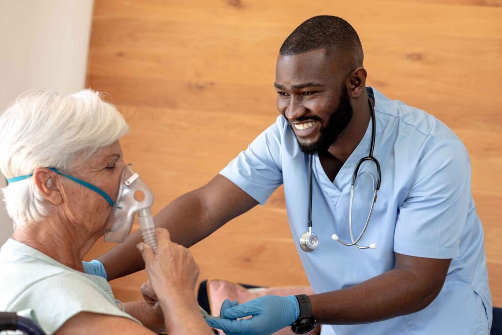 A male respiratory therapist adjusts a breathing mask for an older Caucasian patient, illustrating compassionate care under ‘Respiratory Therapist Staffing.|Importance of respiratory therapists
